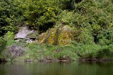 The stream flows into the river on a summer day. Stock Photos