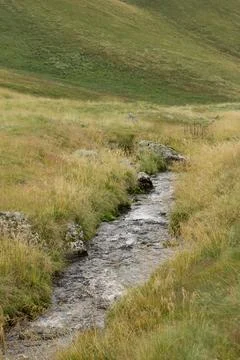 A stream flows through a grassy valley, surrounded by Georgian mountains Stock Photos