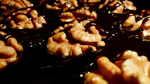 Stream of liquid dark chocolate is poured over roasted walnuts. Close-up. Video stock 149159839