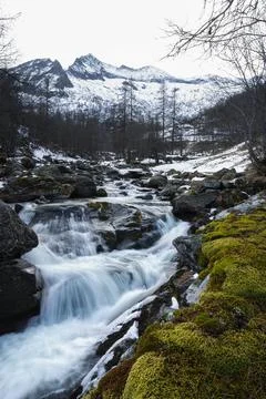 Stream long exposure over the rocks and snowy mountains in background Stock Photos
