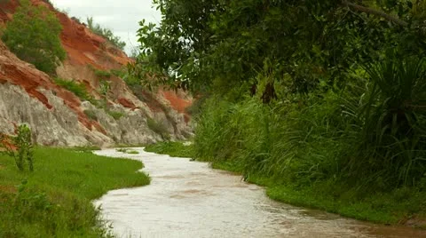 Stream meanders past rocks and red and white sand dunes in river canyon. Video stock 11436322