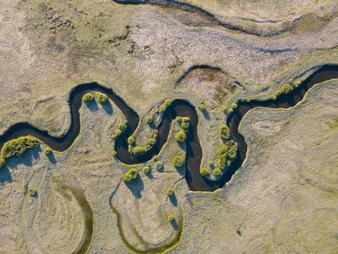 A stream meanders through a green valley, with natural twists and curves. Aerial Stock Photos