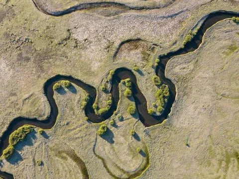 A stream meanders through a green valley, with natural twists and curves. Aerial Stock Photos