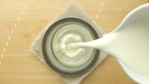 A stream of milk flows into a glass from a white jug, top view, slow-motion vide Stock Footage 236033664