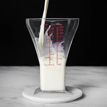 A stream of milk pours into triangle shaped measuring glass Stock Photos