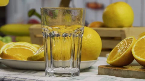 Stream of orange juice falling into wet, glass cup near fruit on kitchen counter Stock Footage 341266570