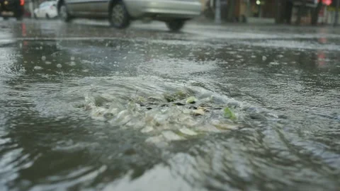 A stream of rainwater flows into the storm drain cars are driving in the Stock Footage 204948560