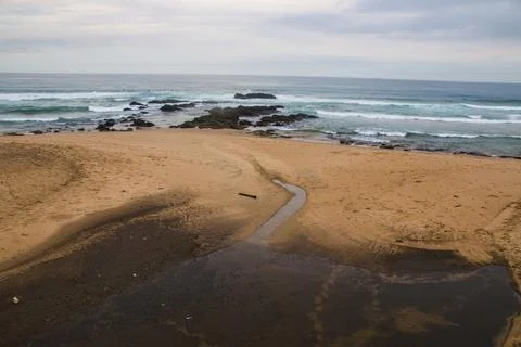 Stream Running onto Beach with Waves and Rocks in Background Stock Photos