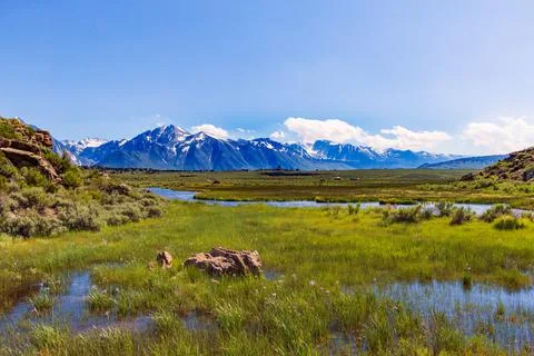 A stream running through a meadow with snowy mountains Stock Photos