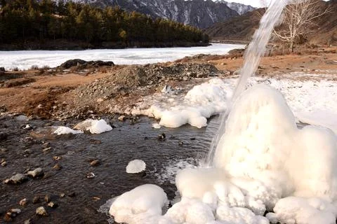 A stream of a small mountain stream flows down onto an ice block of frozen .. Stock Photos