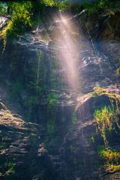A stream of sunlight passes through the mist formed by the waterfall Stock Photos
