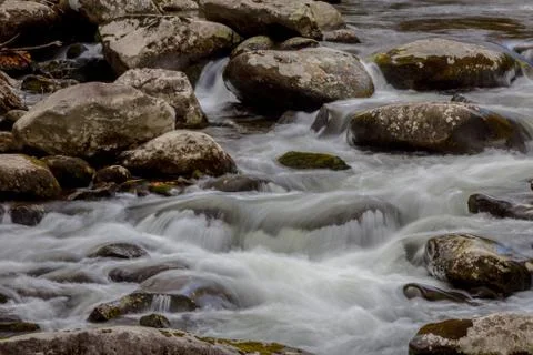 Stream with touches of blue reflections, fall leaves, water flowing over rock Stock Photos