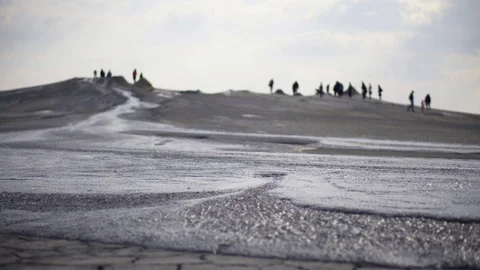 Stream of volcano mud flowing on dried soil. Tourists walking near craters. Stock Footage 105176289