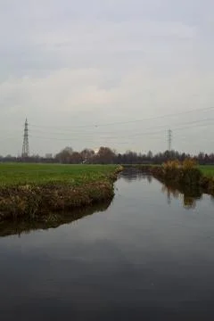 Stream of water between cultivated fields on an overcast day in the italian.. Stock Photos