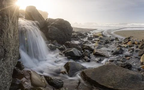A stream of water flows between large rocks on a beach Stock Photos