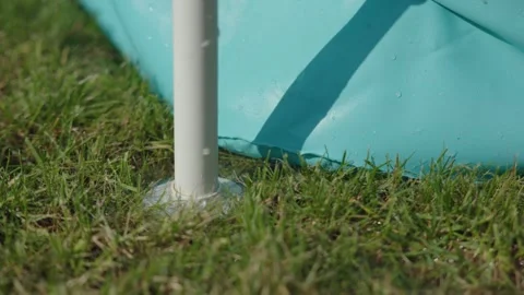 Stream of water flows out of hole in blue inflatable pool on green grass Stock Footage 279515065