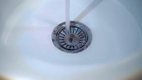 A stream of water flows into a shiny chrome drain in a white sink  Stock Footage 303169169