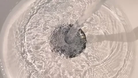 A stream of water flows into a shiny chrome drain in a white sink  Stock Footage 303171170