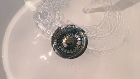 A stream of water flows into a shiny chrome drain in a white sink Stock Footage 303179264