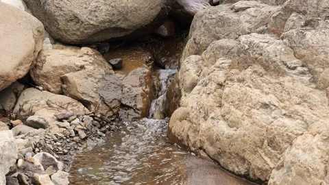 Stream of water flows from underneath rocks, creating serene natural scene Stock Footage 278029397