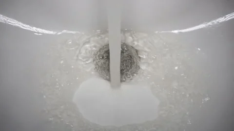 A stream of water flows in a white sink pouring into a pit with a shiny stainles Stock Footage 122209808