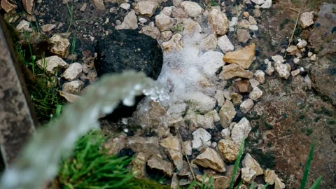 A stream of water pours from a spring pipe onto the rocks on the ground Stock Footage 340138693