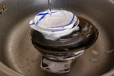 A stream of water pours onto a stack of dirty soapy dishes Stock Photos