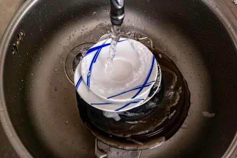 A stream of water pours onto a stack of dirty soapy dishes Stock Photos