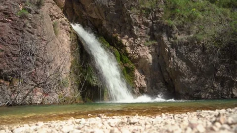 Stream of waterfall flows down mountain over mossy stone, flows into clear river Video stock 262499722