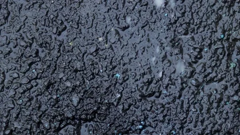 Streams and drops of water from the rain pour onto the black asphalt road with Stock Footage 303136685