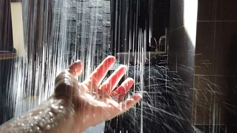 Streams of water from the shower fall on his hand through the sunlight. Stock Footage 107965363