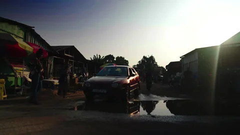 Street with car passing puddle, sun right, Ouesso 库存影片 338167774