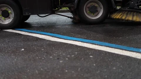 Street cleaning brushes spin fast over wet asphalt scrubbing faded blue and whit Stock Footage 307700516