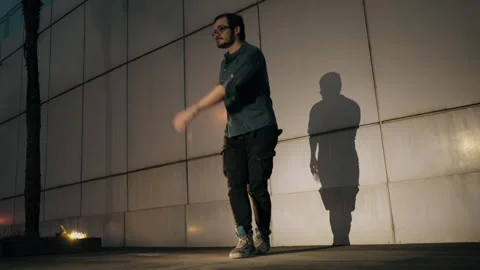 Street dancer performing freestyle moves at night against a concrete wall with Stock Footage 303645994