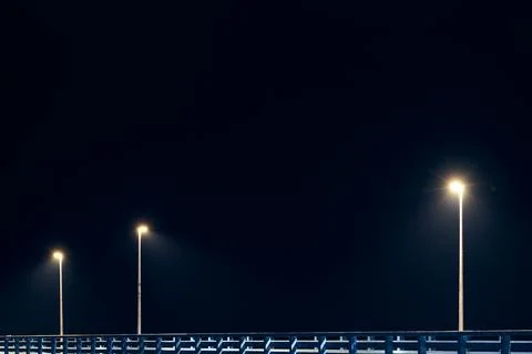 Street lampposts casts dim cold blue glow along shore pier standing against.. Stock Photos