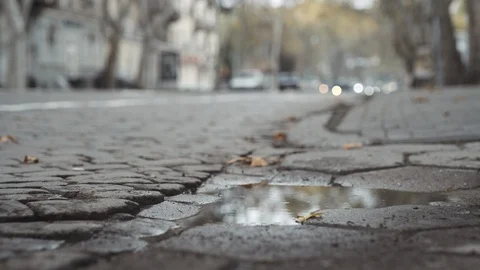 Street-level view of puddle on cobblestone road with traffic out of focus Odessa Stock Footage 122544069