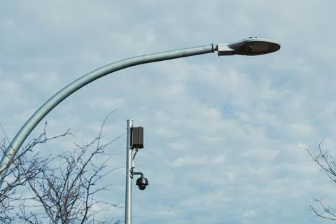 Street light and security camera stand under cloudy sky near urban area dur.. Foto stock