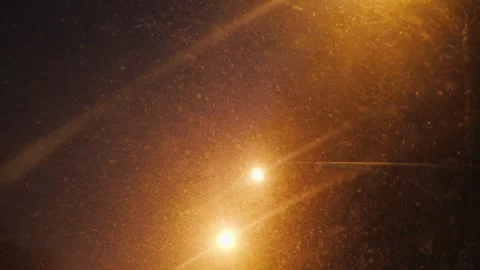 Street lights glow through falling snow at night creating a magical winter .. Видео 334837570