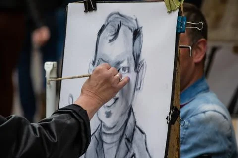 Street painter artist draws a cheerful portrait caricature of a man, hand wit Stock Photos