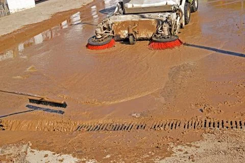 A street sweeper and a worker dump mud from floodwaters into a sewer. Stock Photos