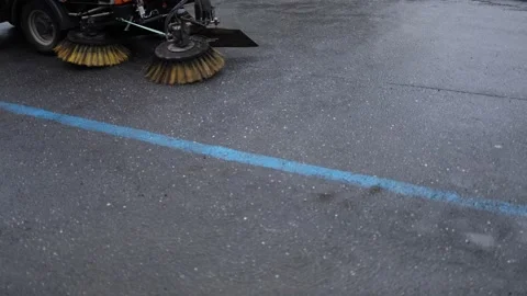 Street sweeper brushes glide across wet asphalt cleaning along faded blue parkin Stock Footage 307700489