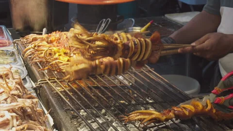 Street vendor is grilling squid satay at a food market Video stock 337950004