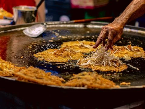 Street Vendor Hand Adding Bean Sprouts to Crispy Thai Oyster Omelette on Ho.. Stock-Fotos