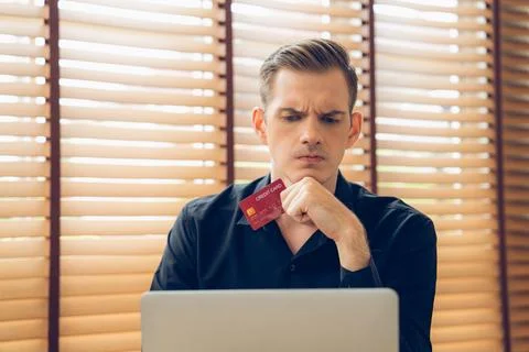 Stress young man sit at at table, pay credit card debt. Unveiling Stockfoto's