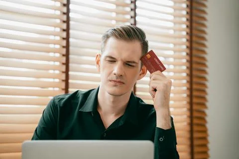 Stress young man sit at at table, pay credit card debt. Unveiling Stockfoto's