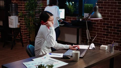 Stressed employee doing multitasking, answering phone while crosschecking data Stock Footage 263382499