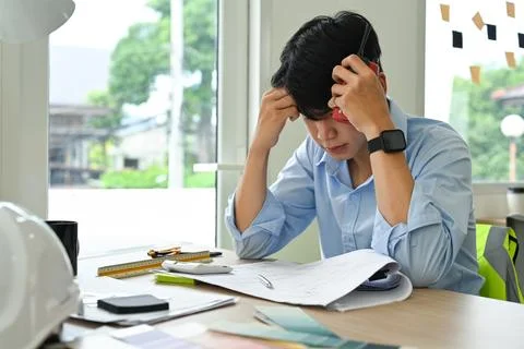 Stressed engineer man working with blueprints, examining construction plans at Foto stock