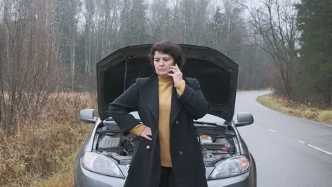 Stressed female driver standing in front of open hood and call evacuation. Stock Footage 144064562