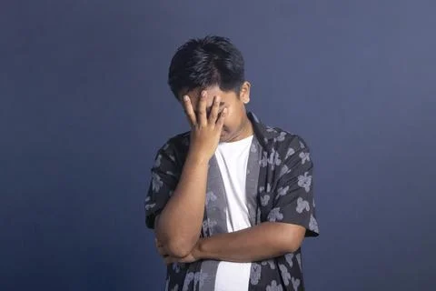 Stressed Indonesian man looking down while covering his face with one hand .. Stock Photos