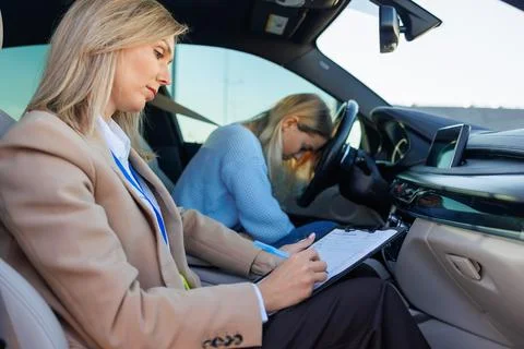 Stressed Learner Driver During Practical Exam with Instructor Taking Notes Foto stock